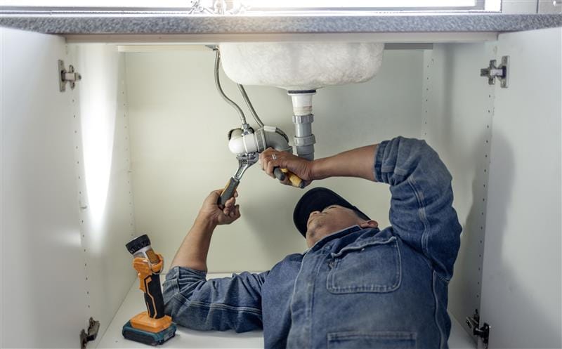 Plumber repairing pipes beneath a bathroom sink in Costa Mesa